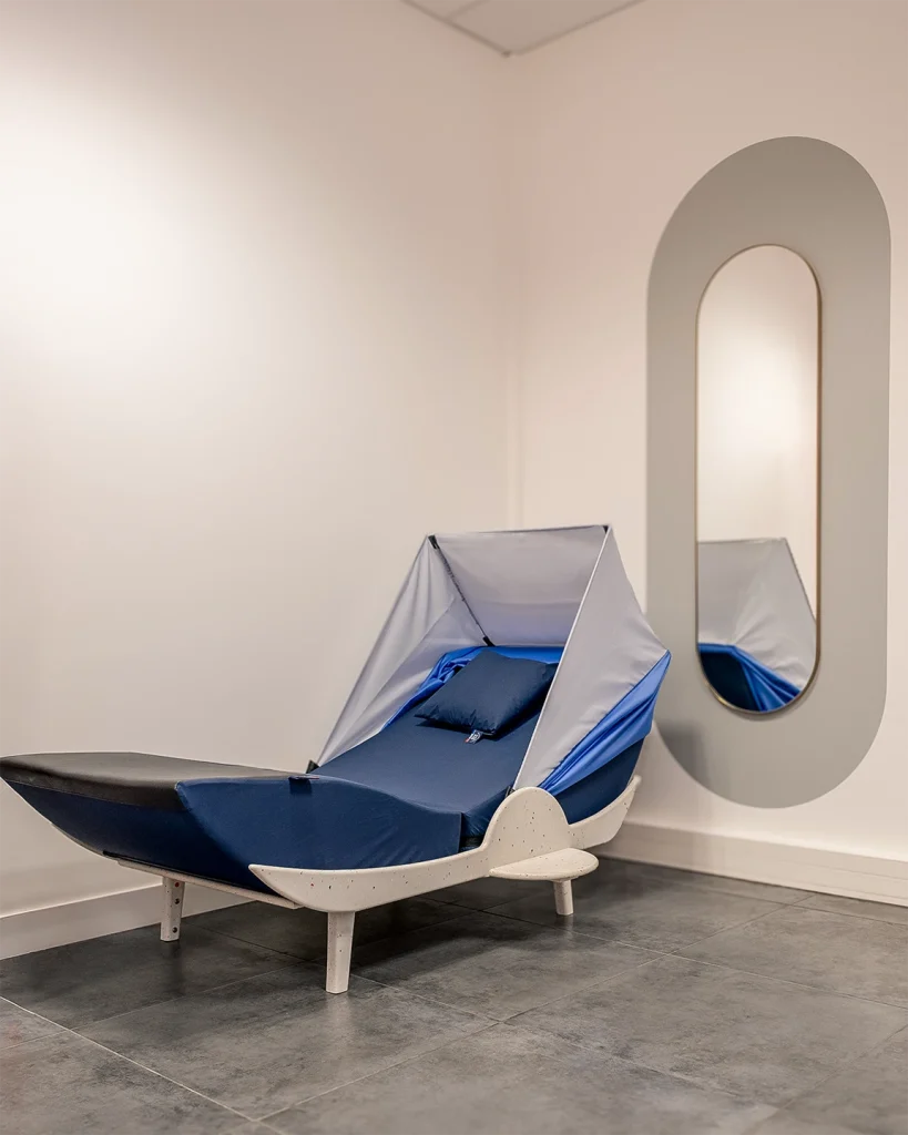 Cocon de sieste bleu marine et gris devant un mur blanc avec un grand miroir ovale