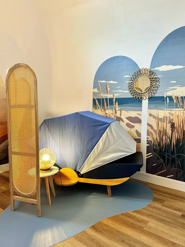 Cocon de repos bleu marine sur un tapis, installé devant une fresque murale thème plage et dunes