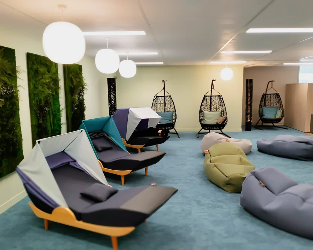 Grand espace détente en entreprise avec fauteuils de sieste, fauteuils suspendus et poufs colorés