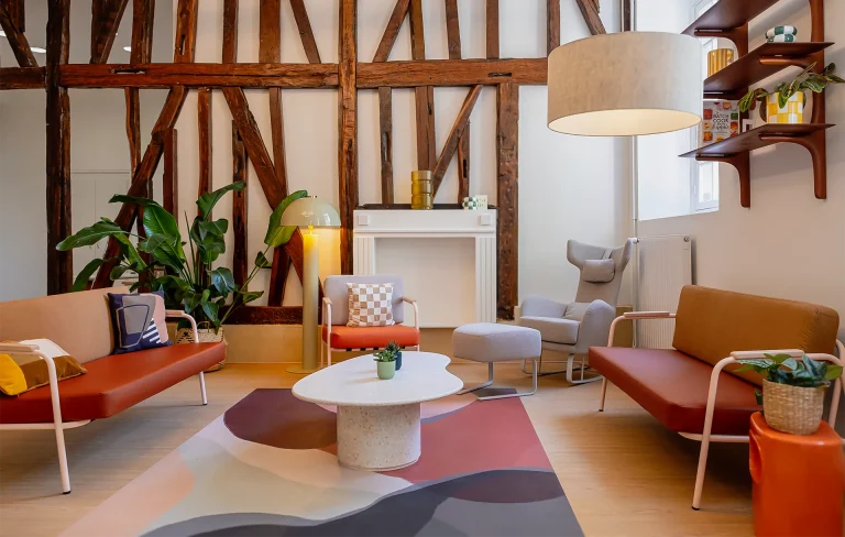 Espace détente confortable alliant poutres en bois anciennes, mobilier moderne coloré et tapis graphique